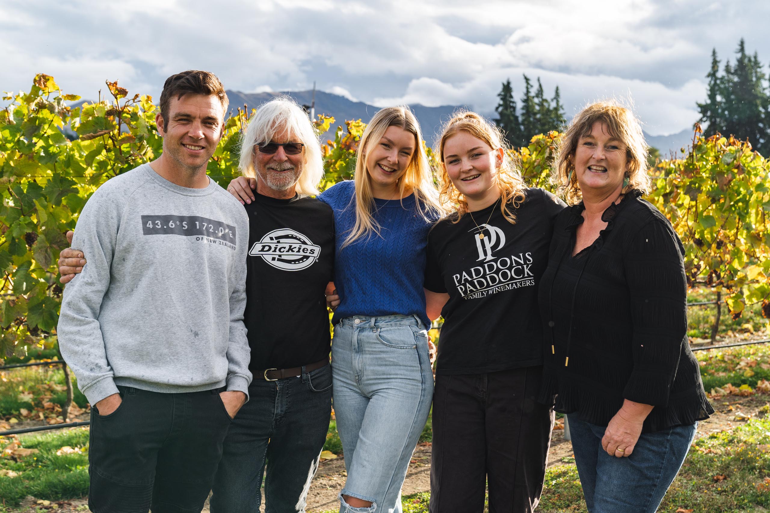 Five people posing together in a vineyard with mountains in the background